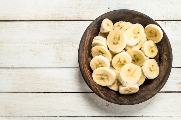 Bananas fatiadas em uma tigela de madeira na mesa de madeira branca.