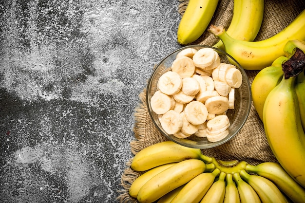 Bananas frescas com pedaços de bananas fatiadas em uma tigela na mesa rústica.