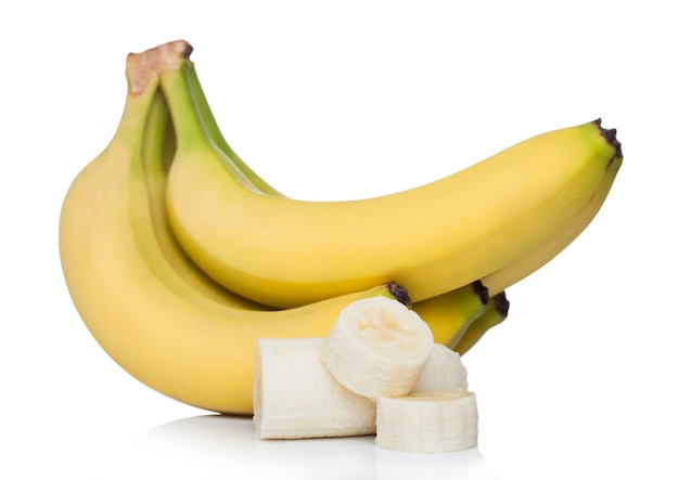 Bananas orgânicas maduras frescas agrupadas com pedaços fatiados na superfície branca