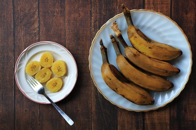 Bananas saba cozidas no vapor em pratos brancos no café da manhã com fundo de mesa de madeira marrom