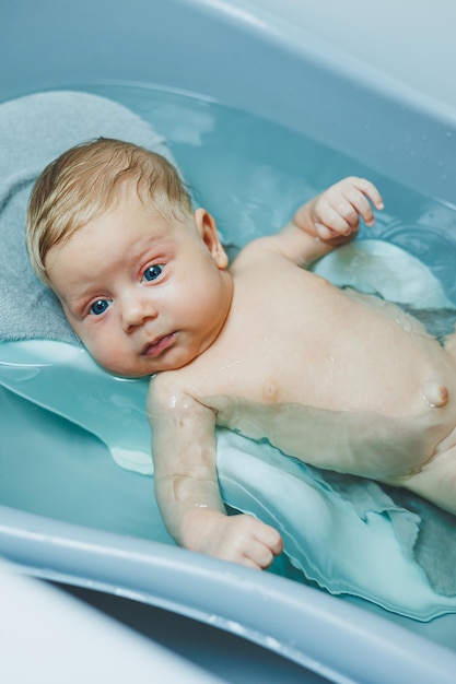 Bañando a un bebé de dos meses en una bañera el niño yace en un soporte de plástico cuidado del bebé