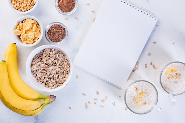 Bananen-Smoothie in Tassen, Leinsamen, Kakao, Haferflocken und Puffreis auf weißem Hintergrund. Konzept für gesunde Ernährung