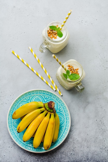 Bananen-Smoothie mit Müsli, getrockneten Früchten und Minze auf grauer Betonoberfläche. Draufsicht.