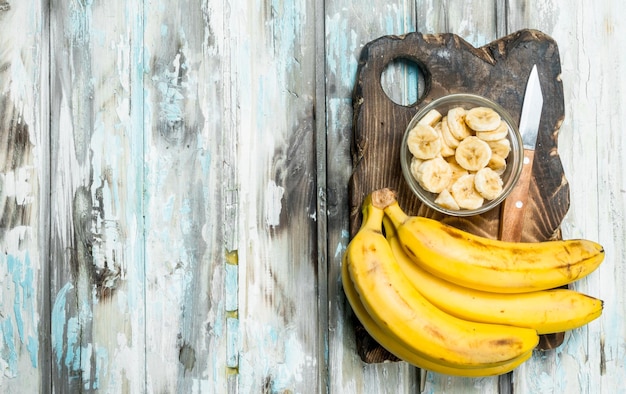 Bananen und Bananenscheiben in einer Glasschüssel auf einem alten Schneidebrett