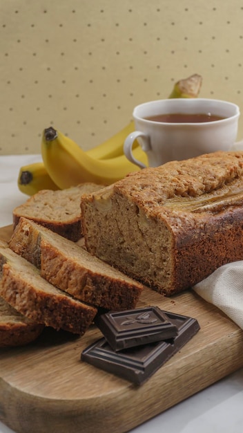 Bananenbrot liegt auf hellem Hintergrund, umgeben von Zutaten zum Kochen und einer Tasse Tee