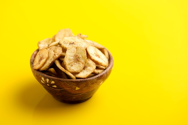 Bananenchips in Holzschale auf gelbem Hintergrund