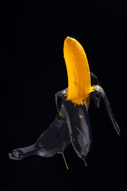 Bananenfarbe. Gelb-schwarz gemalte Banane auf schwarzem Hintergrund Levitation