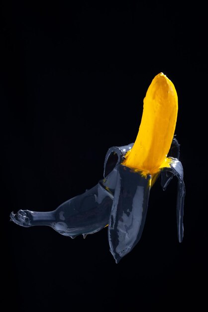 Bananenfarbe. Gelb-schwarz gemalte Banane auf schwarzem Hintergrund schweben.