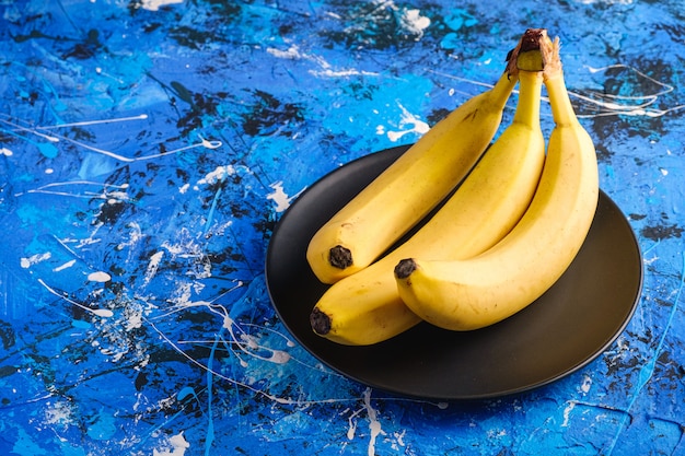 Bananenfrüchte in schwarzer Platte auf blauer strukturierter Oberfläche