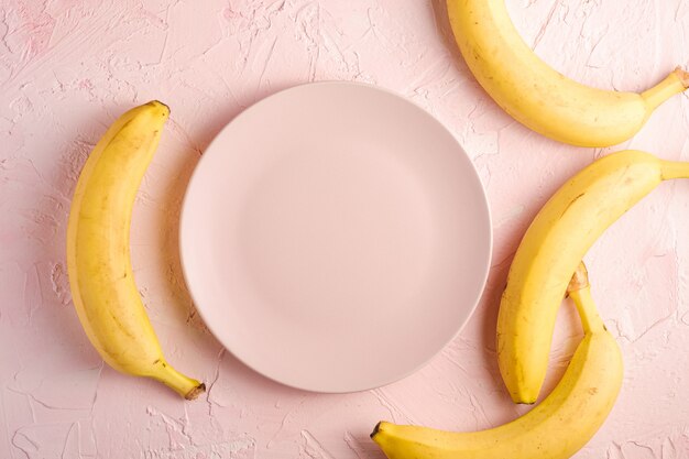 Bananenfrüchte mit leerem rosa Teller auf rosa strukturiertem Hintergrund, Kopierraum der Draufsicht