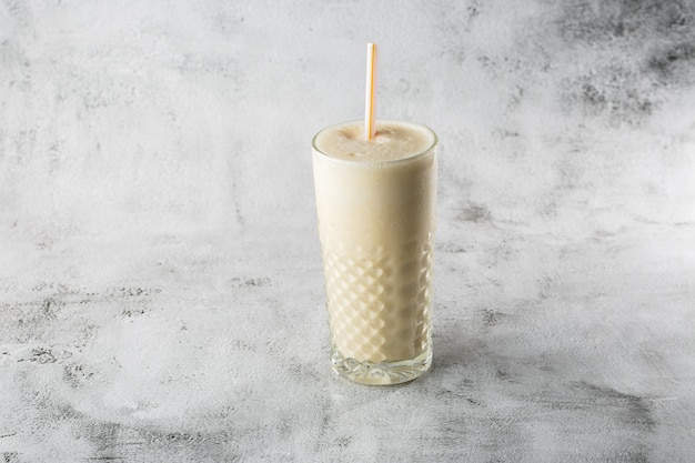 Bananenhafer-Smoothie oder Vanillemilchshake im Glas auf hellem Marmorhintergrund. Draufsicht, Speicherplatz kopieren. Werbung für Milchshake-Café-Menü. Horizontales Foto.