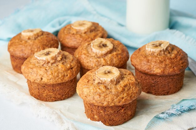 Bananenmuffin, Seitenansicht, Abschluss oben. Kleine Kuchen auf blauer Serviette mit Milch im bittle, weißen Beton