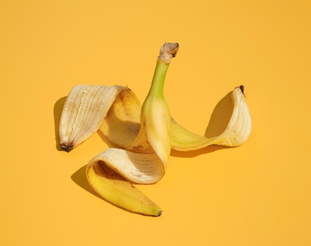 Bananenschale liegt auf gelber Oberfläche. Gesundheitsgefahr, lächerliche Situation.