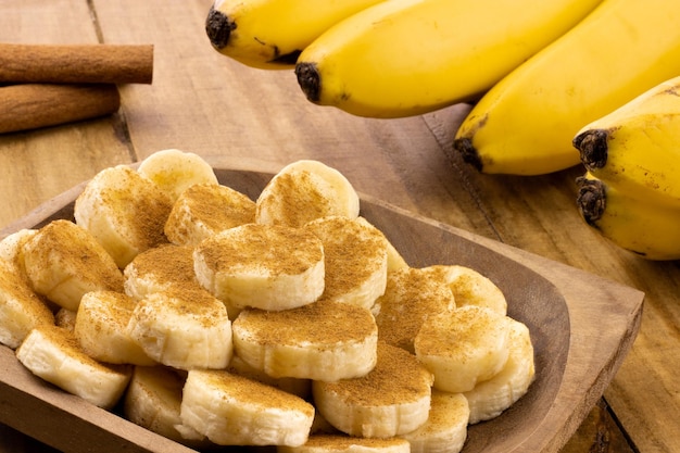 Bananenscheiben mit Zimt bestreut und Zimtstangen mit Bündel Bananen im Hintergrund