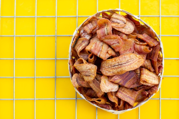 Bananenscheibenchips im Bambuskorb auf gelbem Hintergrund