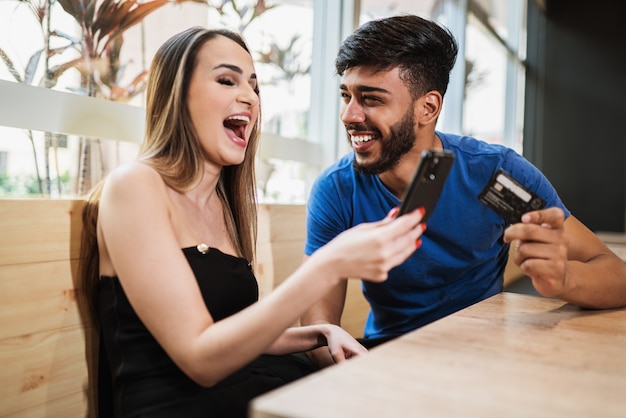 Banca en línea de pareja joven usando teléfonos inteligentes comprando en línea con tarjeta de crédito en el balcón de su estilo de vida hogareño