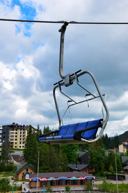 Banco de elevador vazio em movimento em uma montanha em azul sobre um fundo desfocado dos edifícios de uma estância turística de verão e o céu azul com nuvens.