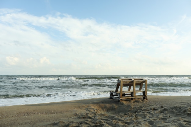 Banco de madeira na areia da praia do mar, espaço para texto