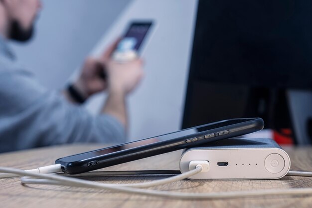 Banco de potência com um telefone e um cabo no fundo de um homem sentado em frente ao monitor.
