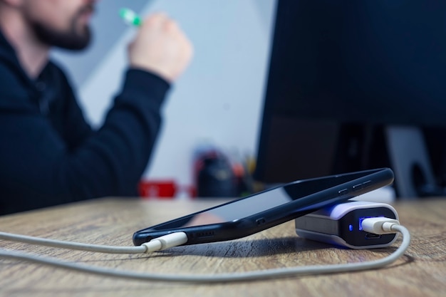 Banco de energía con un teléfono y un cable en el fondo de un hombre sentado en el monitor.