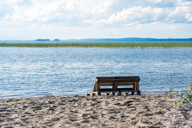 banco hecho de viejos paletes en una orilla de arena de un vasto lago