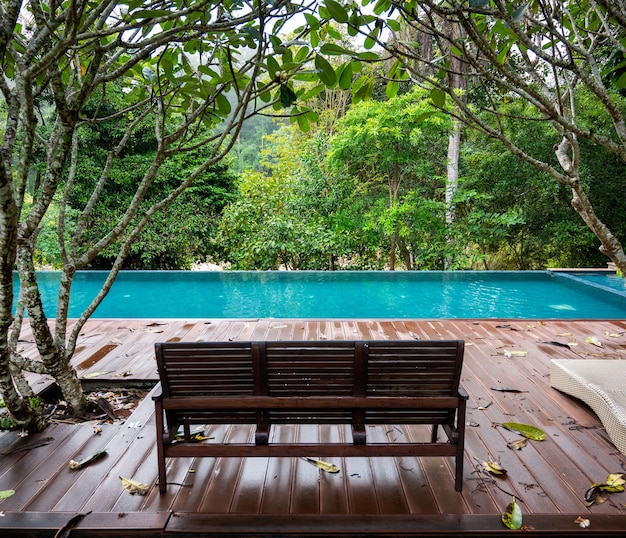 Banco de madera en casa junto a la piscina con una cálida lluvia de selva tropical cayendo en Tailandia.