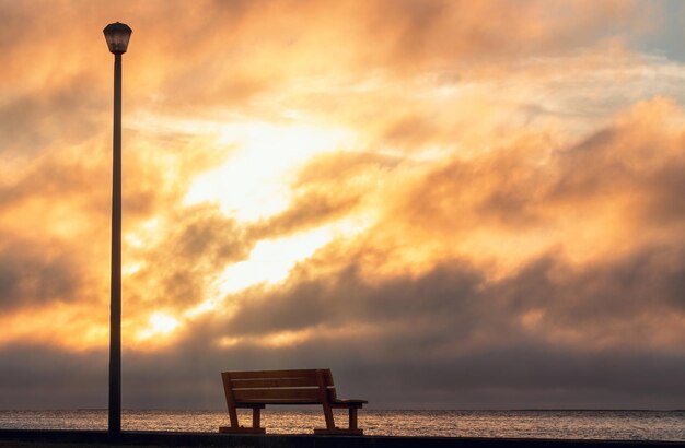 Un banco de madera y una lámpara de calle con una vista de fondo de una puesta de sol brillante