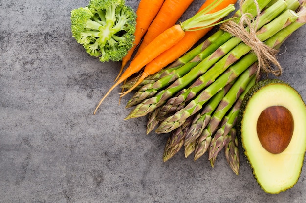 Bancos de espárragos verdes frescos y verduras sobre superficie de hormigón, vista superior