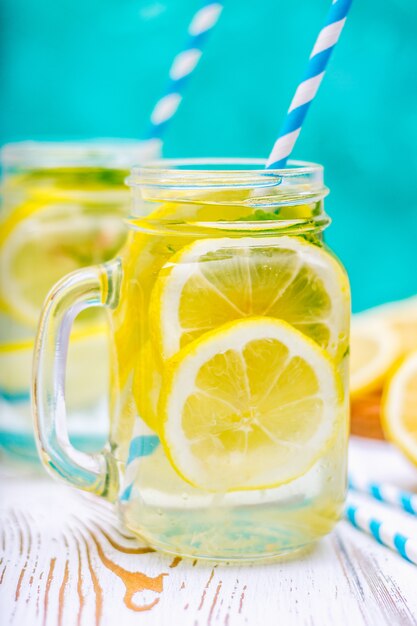 Bancos con las manijas con limonada fría en un fondo de madera blanco. Limones