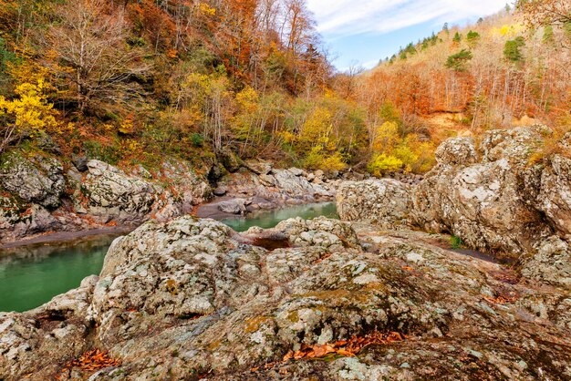 Bancos rochosos de granito de um rio de montanha e floresta de outono