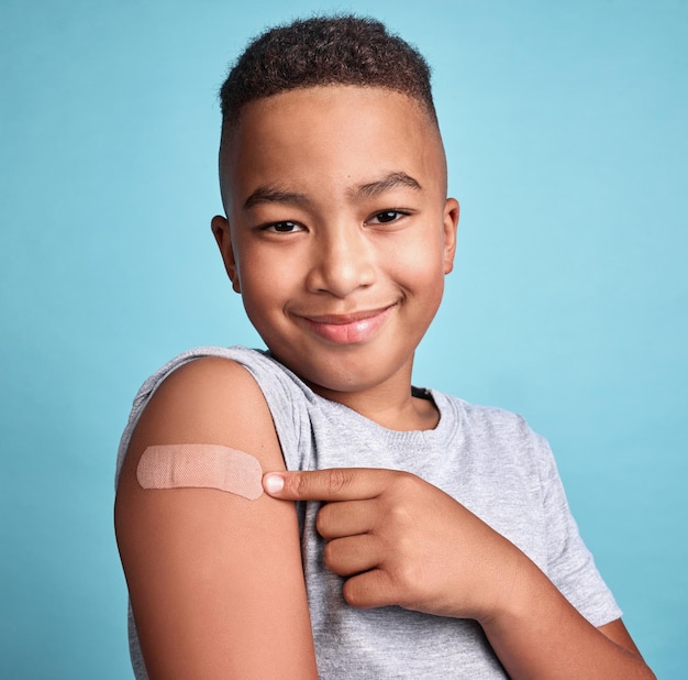 Foto band-aid preto infantil e criança feliz com vacina em fundo de estúdio azul e relaxe com sorriso ou alegre retrato de menino e bandagem adesiva com hematoma no braço confiante e vacinação para a saúde