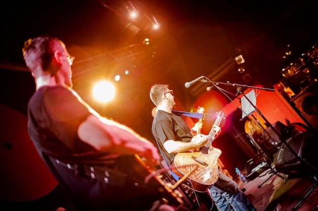 Band tritt auf der Bühne auf, Rockkonzert in einem Nachtclub. Authentische Aufnahmen mit hohem ISO-Wert bei schwierigen Lichtverhältnissen. Ein wenig Körnung und unscharfe Bewegungseffekte.