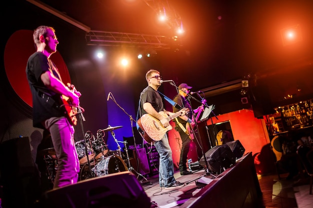 La banda actúa en el escenario, un concierto de música rock en una discoteca. Disparos auténticos con alta iso en condiciones de iluminación desafiantes. Un poco de grano y efectos de movimiento borrosos.