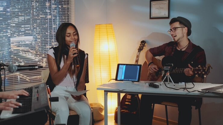 Banda moderna ensayando en estudio casero: joven tocando la guitarra y una niña de raza mixta cantando en el micrófono