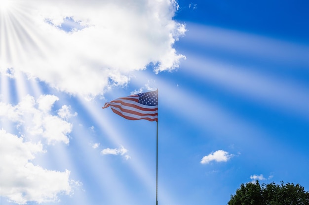 Bandeira americana acenando em um céu nublado e raios de sol. A bandeira dos EUA voa