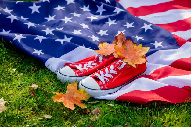 Bandeira americana com folhas de bordo e sapatos desportivos vermelhos na grama verde no outono