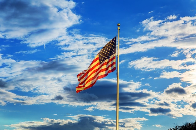 Bandeira americana voando na brisa contra um céu azul com nuvens brancas