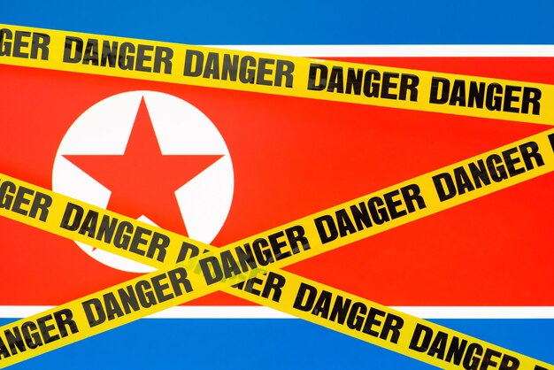 Bandeira da Coreia do Norte com fita de perigo em primeiro plano