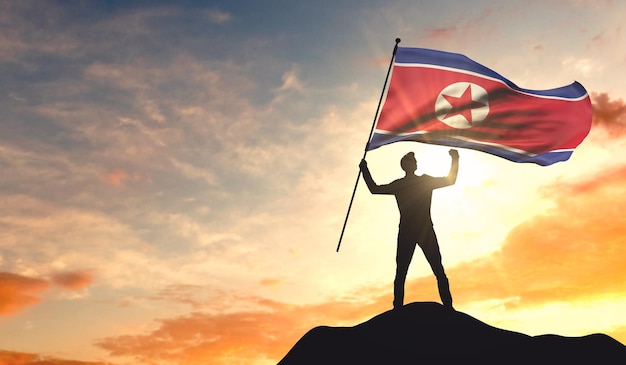 Bandeira da Coreia do Norte sendo acenada por um homem comemorando o sucesso no topo de uma montanha 3D Rendering