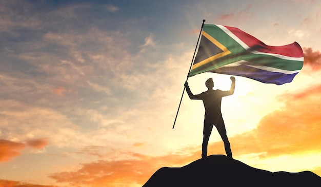 Bandeira da África do Sul sendo acenada por um homem comemorando o sucesso no topo de uma montanha 3D Rendering