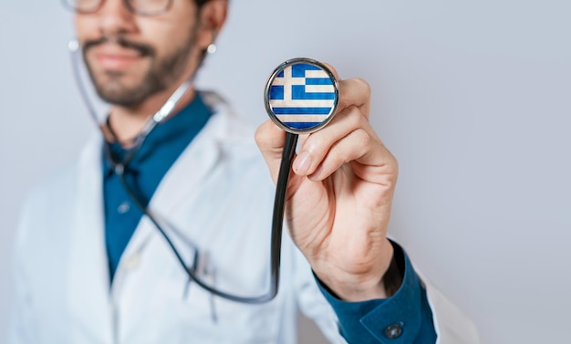 Bandeira da grécia no estetoscópio médico segurando o estetoscópio com bandeira da grécia médico masculino mostrando o estetoscópio com bandeira da grécia