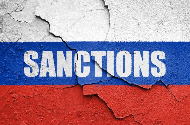 Bandeira da Rússia pintada em uma parede com a palavra SANCTIONS Embargo e sanções por agressão militar