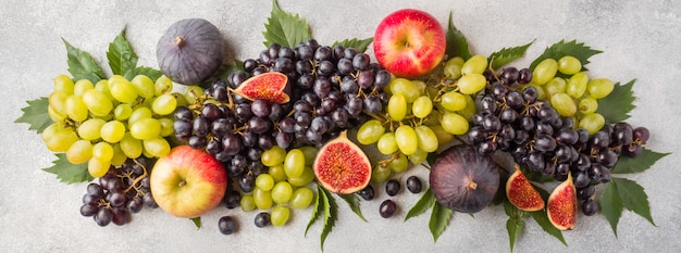 Bandeira de frutas frescas do outono. Uvas preto e verde, figos e folhas em uma mesa cinza.