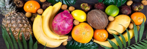 Bandeira de frutas tropicais do arco-íris saudável com palma deixa na mesa de madeira azul