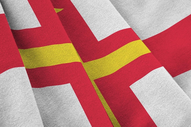 Bandeira de guernsey com grandes dobras acenando sob a luz do estúdio dentro de casa os símbolos e cores oficiais no banner