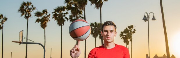 Bandeira de homem esportivo segura bola de basquete na quadra de basquete de praia de veneza bola de basquete girando à mão