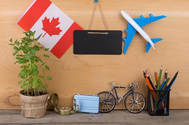 Bandeira de lousa em branco do conceito de tempo de viagem do modelo de avião do Canadá pequena bicicleta e bússola de mala em fundo de madeira