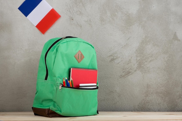 Bandeira de mochila verde da França e material escolar contra uma parede de cimento