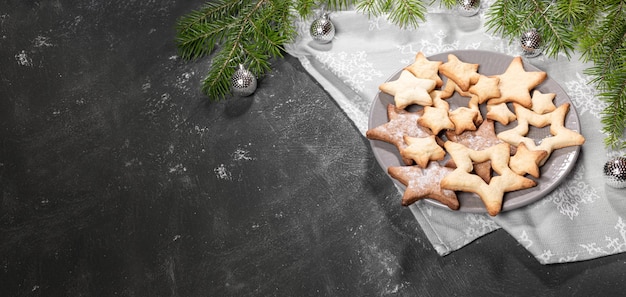 Foto bandeira de natal com biscoitos de cozimento festivo de forma de estrelas com galhos de abeto em preto com espaço de cópia