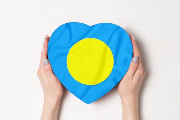 Bandeira de Palau em uma caixa em forma de coração nas mãos femininas. Branco